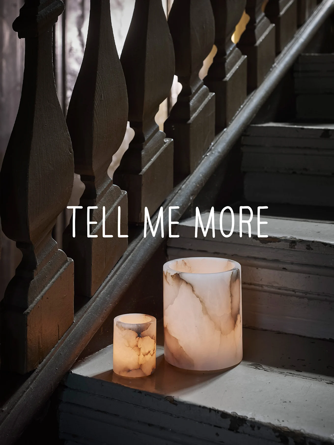 两个发光的缟玛瑙烛台，置于磨损的木制楼梯上，附有“TELL ME MORE”文字。