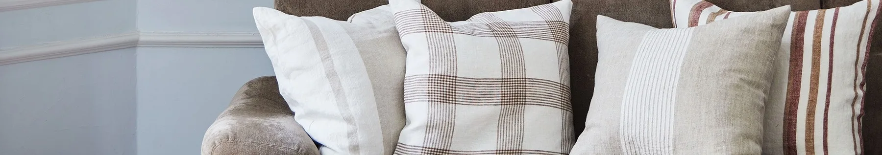 棕色沙发上的三个靠垫特写，图案为白色、米色、格子纹，带有棕色和红色条纹。