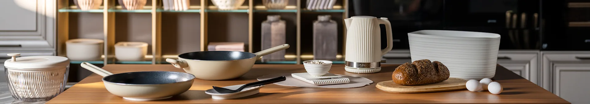 厨房台面，上面有米色平底锅、白色条纹水壶、砧板上的带籽面包和鸡蛋。现代厨房配件。