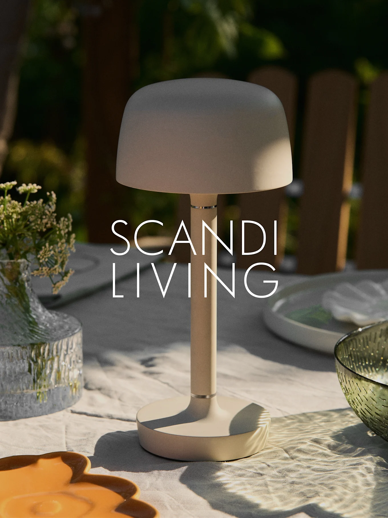 米色现代便携式台灯，置于户外桌上，旁有花瓶和餐具。“SCANDI LIVING”字样。