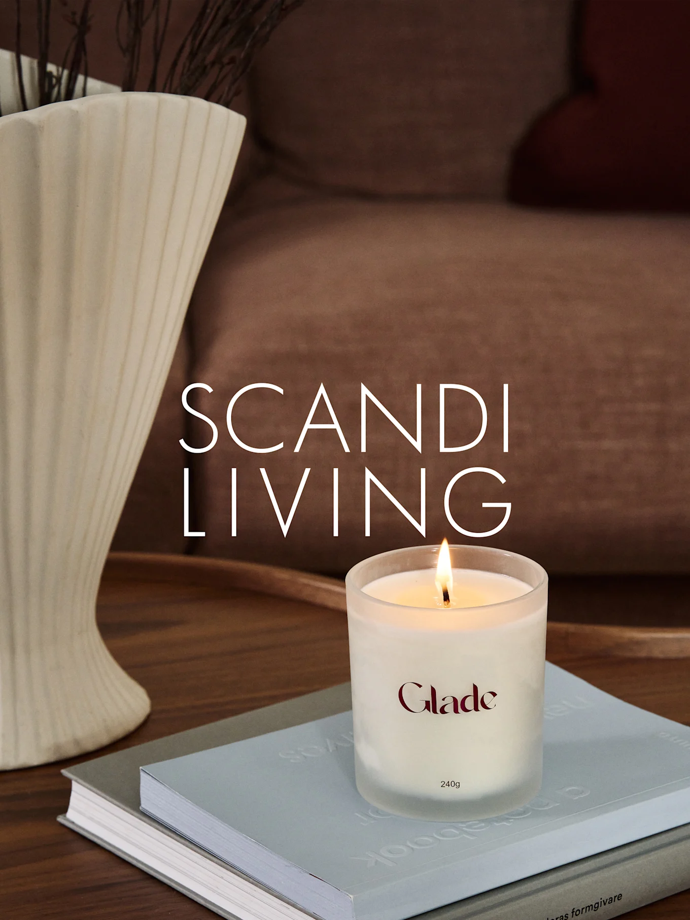 书本上燃着的Glade蜡烛，旁边是插有树枝的带纹理花瓶。叠加文字：SCANDI LIVING。